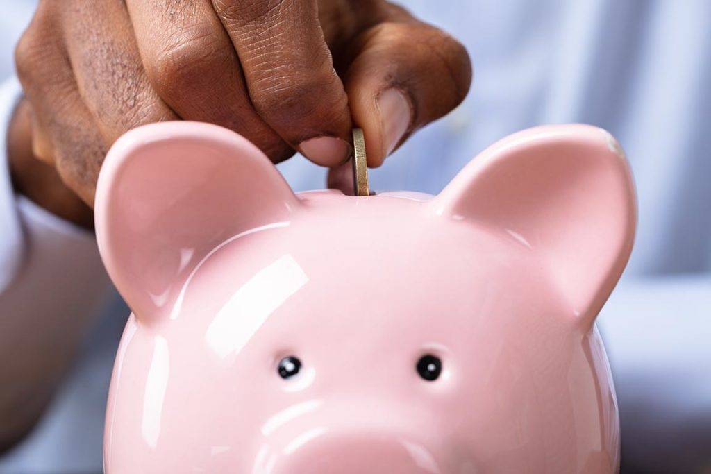 Photo of a person putting coins in a piggy bank.