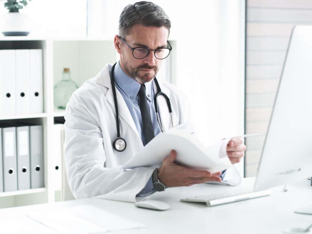 Doctor working at desk considering the cost and benefits of investing in a phototherapy booth for his practice