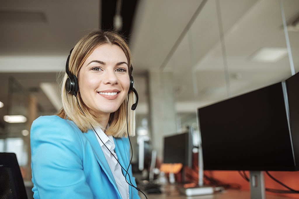 A female sales representative smiling while sitting next to a computer ready to speak with DME Distributors. 